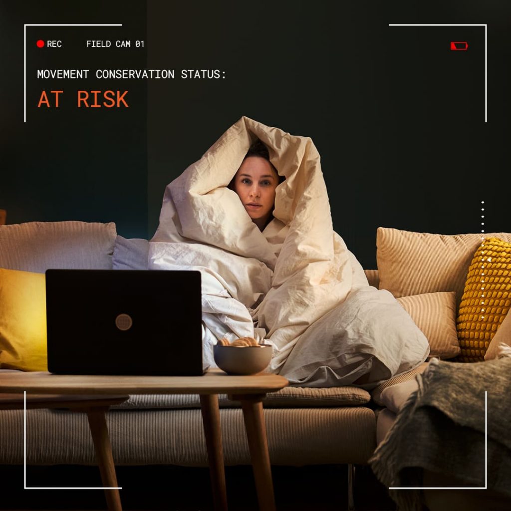 אישה עטופה בשמיכה מול לפטופ על ספה, עם כיתוב At Risk. צילום: באדיבות המותג